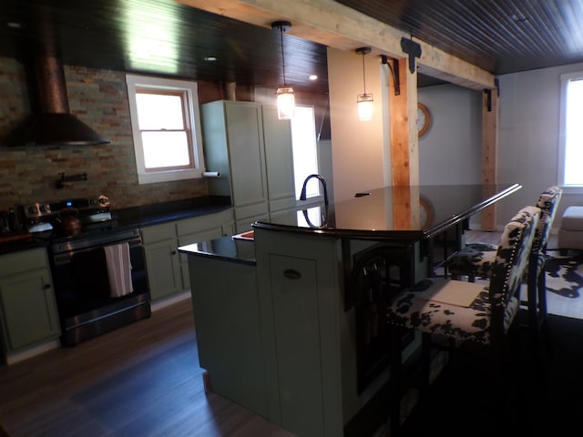 kitchen featuring wall chimney range hood, hanging light fixtures, electric stove, and an island with sink