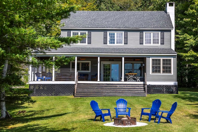 rear view of house with an outdoor fire pit, a deck, and a lawn