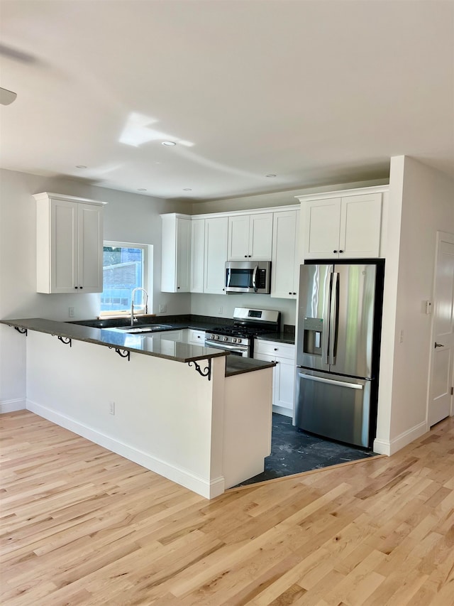 kitchen with appliances with stainless steel finishes, kitchen peninsula, light hardwood / wood-style flooring, and white cabinets