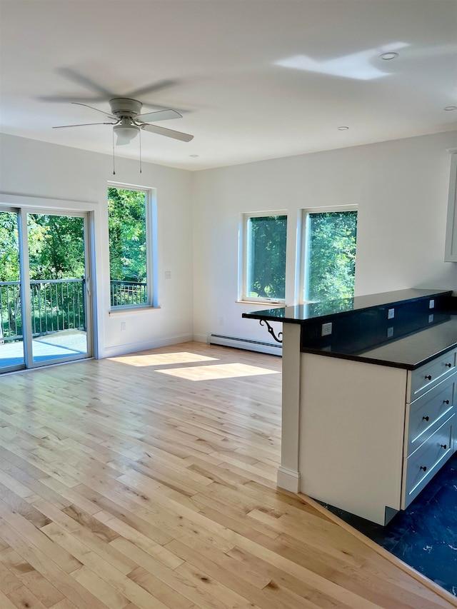 kitchen featuring ceiling fan, a kitchen breakfast bar, white cabinets, a baseboard radiator, and light wood-type flooring