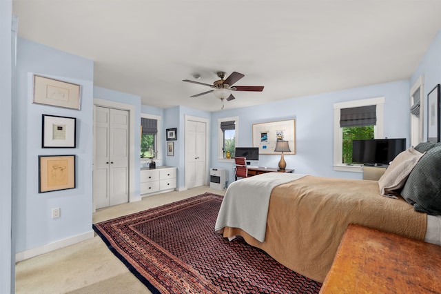 bedroom with heating unit, two closets, ceiling fan, and carpet floors