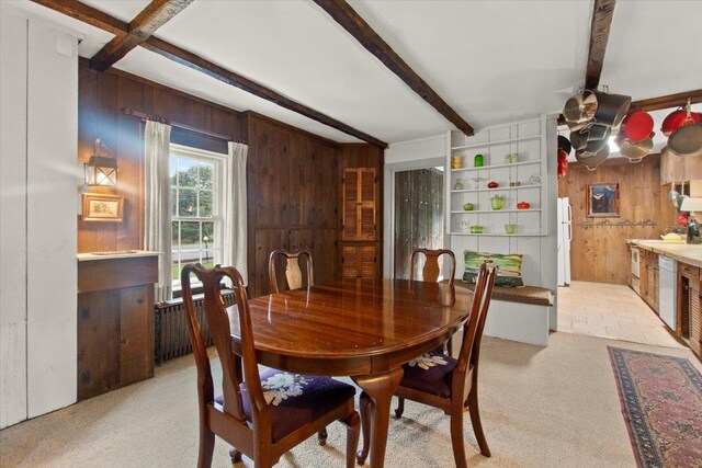 dining room with wood walls, radiator, beam ceiling, and light carpet