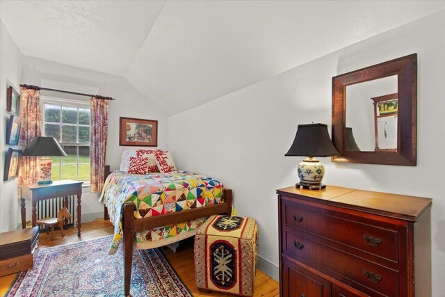 bedroom with vaulted ceiling, radiator heating unit, and light wood-type flooring