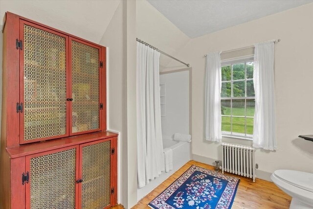 bathroom featuring toilet, shower / tub combo, radiator, lofted ceiling, and hardwood / wood-style flooring