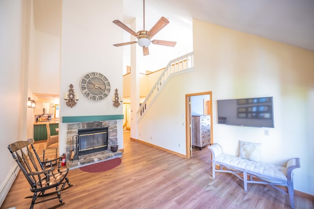 living area with baseboards, stairs, a fireplace, wood finished floors, and a ceiling fan