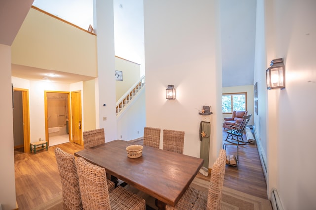 dining room featuring stairway, a baseboard heating unit, a towering ceiling, and wood finished floors