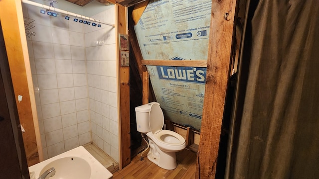 bathroom featuring hardwood / wood-style flooring, tiled shower, and toilet