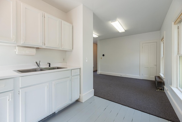 kitchen with baseboards, light countertops, white cabinets, radiator heating unit, and a sink