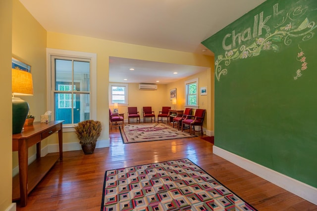living room with wood-type flooring, an AC wall unit, baseboards, and recessed lighting
