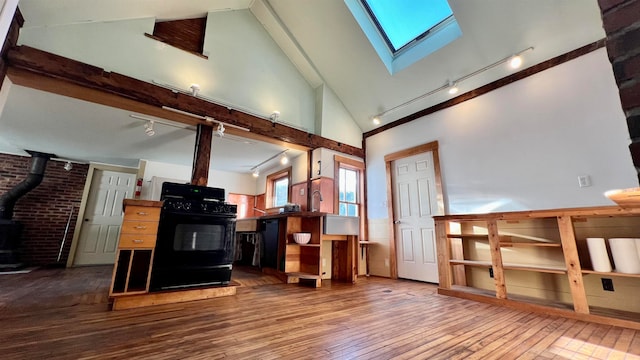 interior space with a skylight, a wood stove, wood-type flooring, black range with gas stovetop, and high vaulted ceiling