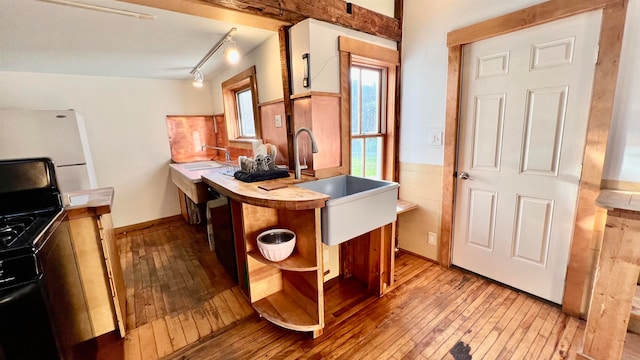 kitchen featuring rail lighting, white fridge, hardwood / wood-style floors, and black gas range oven