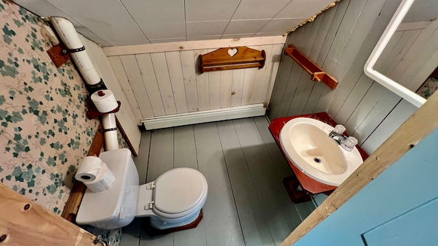 bathroom featuring baseboard heating, toilet, and wooden walls