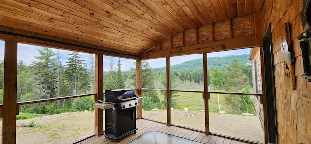 unfurnished sunroom with a wealth of natural light, vaulted ceiling, a mountain view, and wood ceiling