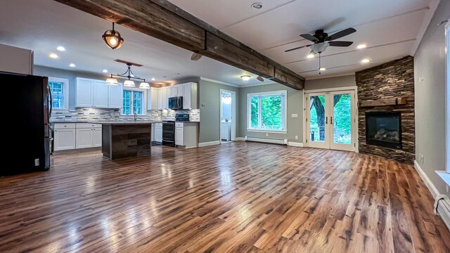 unfurnished living room with dark hardwood / wood-style flooring, a baseboard radiator, a stone fireplace, beam ceiling, and ceiling fan