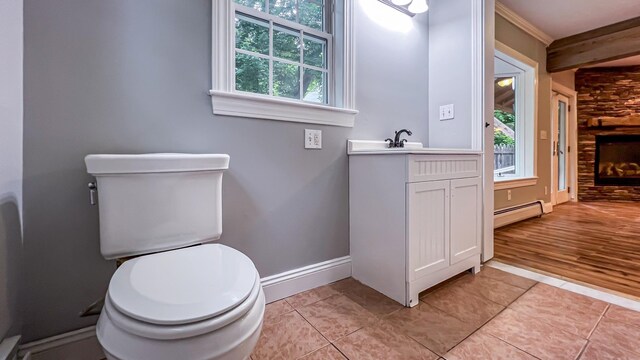 bathroom with a fireplace, toilet, vanity, baseboard heating, and hardwood / wood-style flooring