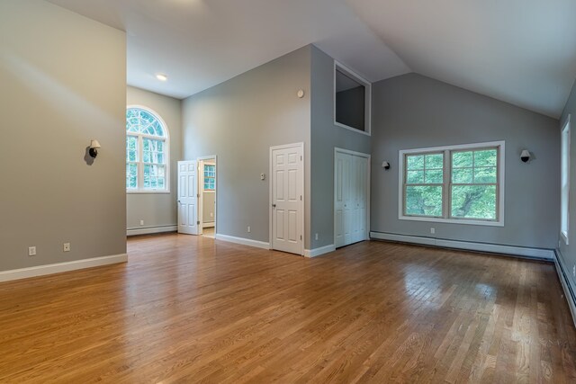 unfurnished living room featuring high vaulted ceiling, baseboard heating, and light hardwood / wood-style flooring