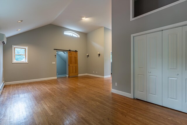 interior space featuring lofted ceiling, hardwood / wood-style flooring, an AC wall unit, and a barn door