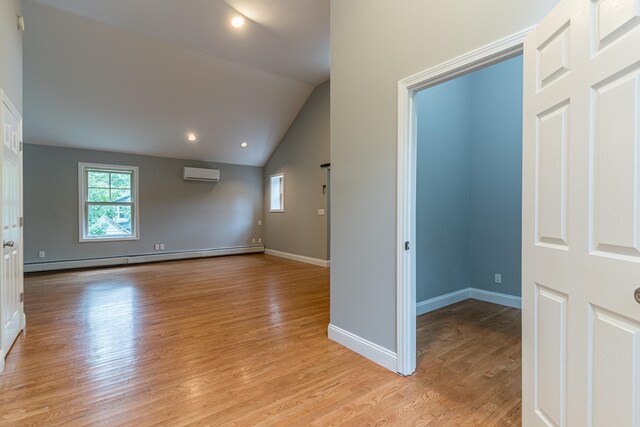 empty room with a baseboard heating unit, vaulted ceiling, light wood-type flooring, and a wall mounted air conditioner