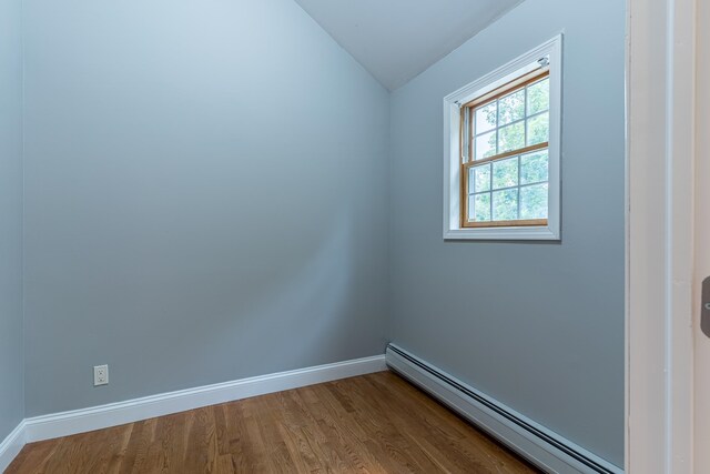 empty room with a baseboard radiator, wood-type flooring, and vaulted ceiling