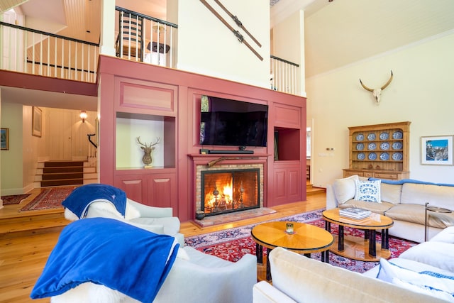 living room featuring light wood-style flooring, stairway, a lit fireplace, crown molding, and a towering ceiling