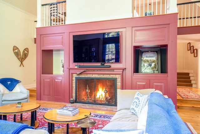 living area featuring wood finished floors, a lit fireplace, crown molding, baseboards, and stairs