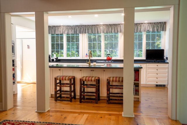 kitchen featuring dark countertops, light wood finished floors, a breakfast bar area, and a sink