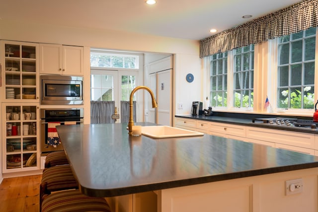 kitchen with light wood finished floors, a sink, stainless steel appliances, dark countertops, and a center island