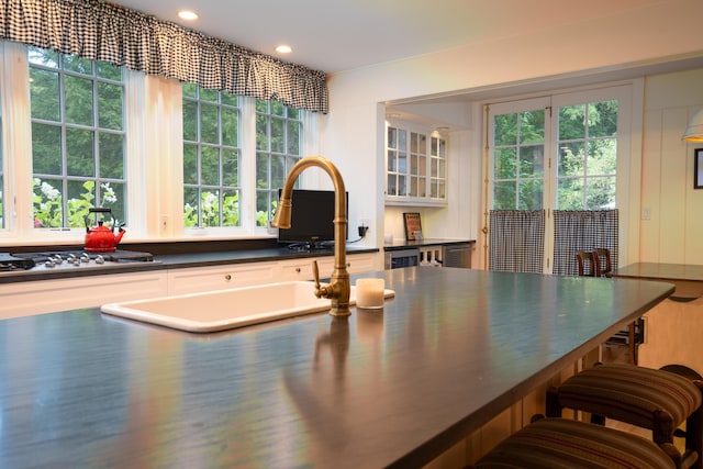 kitchen featuring a sink, a kitchen breakfast bar, dark countertops, glass insert cabinets, and stainless steel gas cooktop