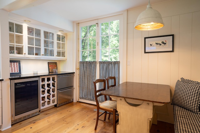 dining space with a bar, beverage cooler, and light wood-type flooring