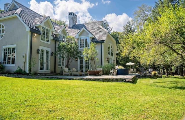 rear view of house with a lawn, french doors, a chimney, and a patio