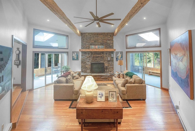 living room with light hardwood / wood-style flooring, ceiling fan, a stone fireplace, high vaulted ceiling, and beam ceiling