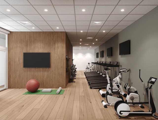 gym with wood walls, a drop ceiling, and light wood-type flooring