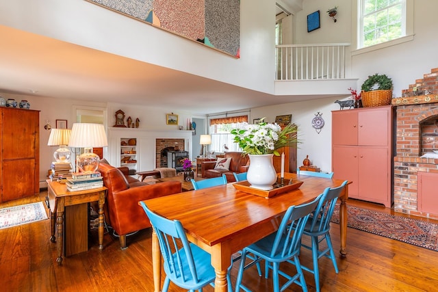 dining space with a high ceiling, wood finished floors, and a brick fireplace