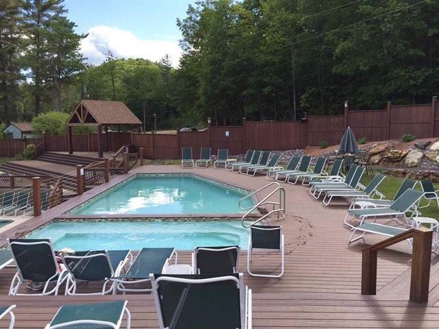 view of pool featuring a hot tub, a deck, and fence