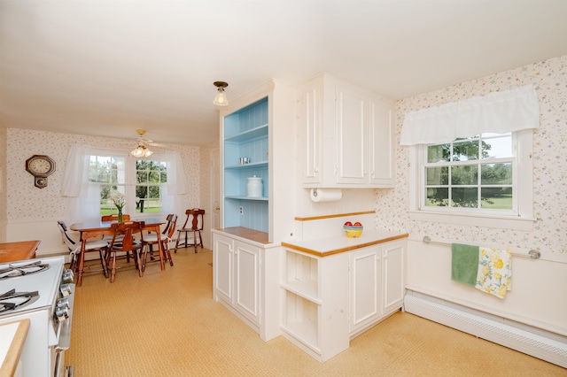 kitchen with white cabinets, baseboard heating, gas range gas stove, ceiling fan, and light colored carpet