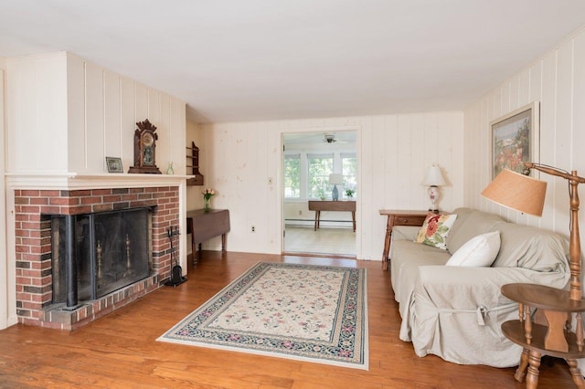 living room with a baseboard heating unit, wood-type flooring, a fireplace, and ceiling fan