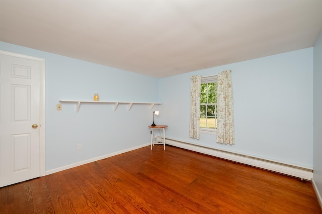 spare room featuring a baseboard heating unit and wood-type flooring