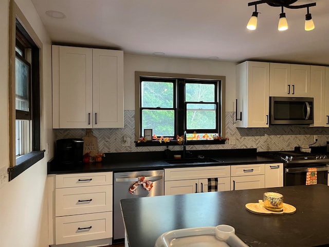 kitchen featuring white cabinets, dark countertops, a sink, stainless steel appliances, and backsplash