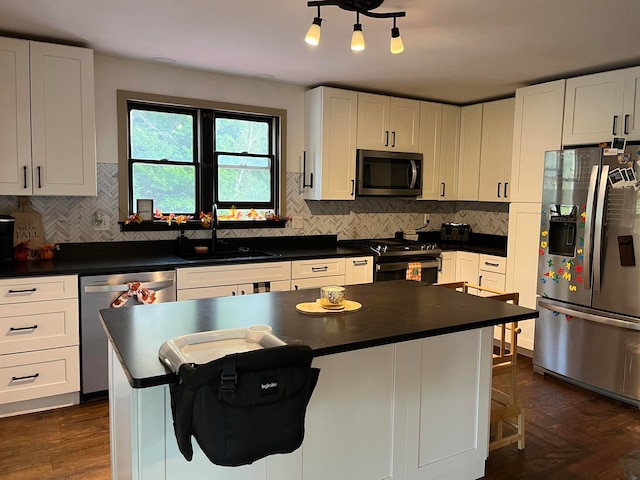 kitchen with dark countertops, appliances with stainless steel finishes, a center island, white cabinetry, and a sink