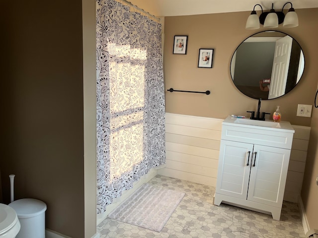 bathroom featuring a wainscoted wall, wood walls, vanity, and toilet