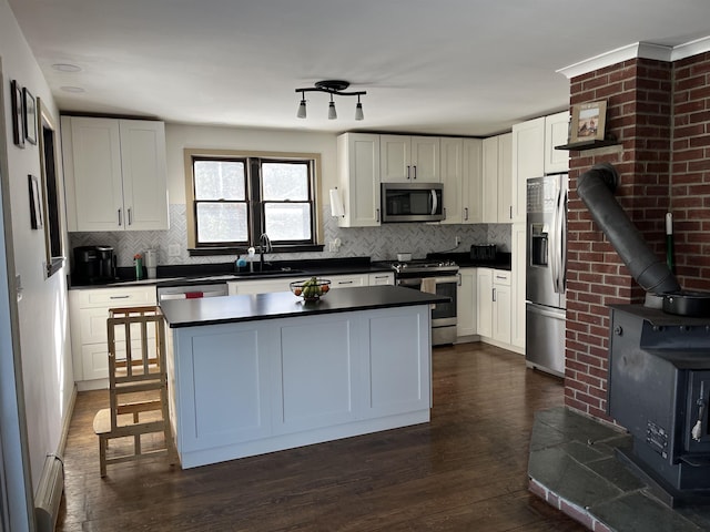 kitchen with a wood stove, dark countertops, appliances with stainless steel finishes, and a sink