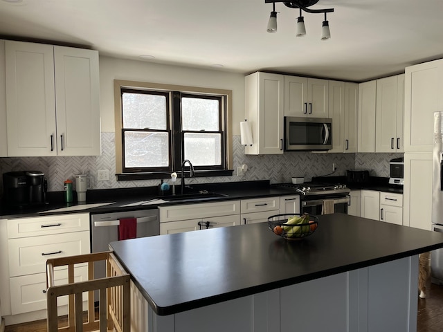 kitchen with appliances with stainless steel finishes, dark countertops, white cabinetry, and a sink