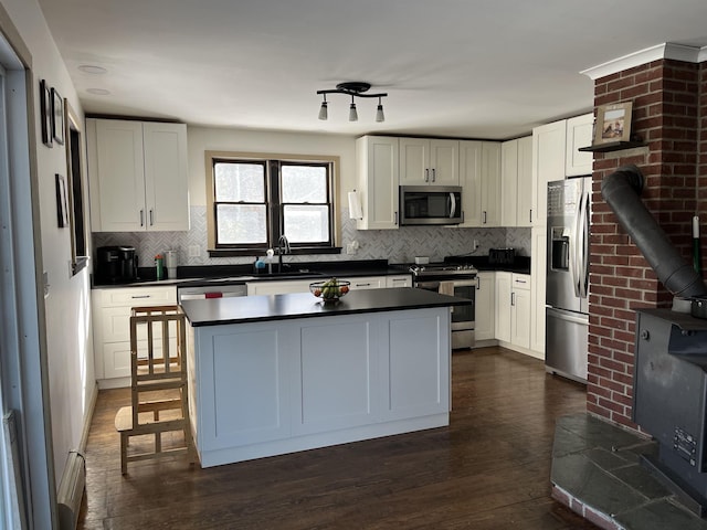 kitchen with dark countertops, appliances with stainless steel finishes, a wood stove, white cabinetry, and a sink