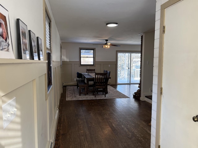 dining space with dark wood-style floors, ceiling fan, a decorative wall, and a wainscoted wall