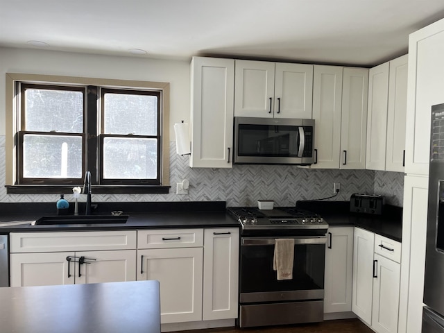 kitchen with appliances with stainless steel finishes, dark countertops, a sink, and white cabinetry