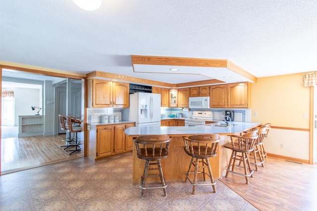 kitchen featuring hardwood / wood-style flooring, white appliances, sink, a breakfast bar, and a textured ceiling