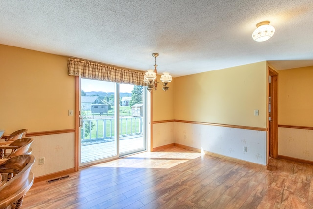 spare room with a textured ceiling, hardwood / wood-style floors, and a notable chandelier