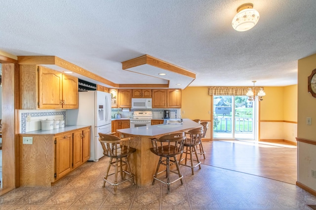 kitchen featuring an inviting chandelier, white appliances, a center island, and a textured ceiling