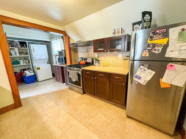 kitchen featuring lofted ceiling, stacked washer and dryer, appliances with stainless steel finishes, backsplash, and dark brown cabinets