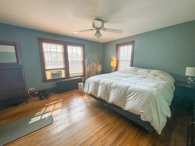 bedroom with hardwood / wood-style floors, radiator heating unit, ceiling fan, and cooling unit